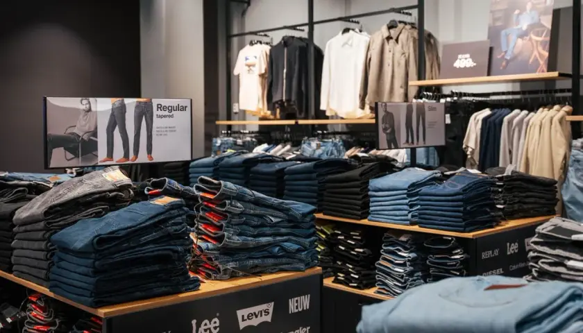 Staplade jeans i olika tvättar och modeller, inklusive "regular tapered" och "slim". En skylt visar olika passformer.