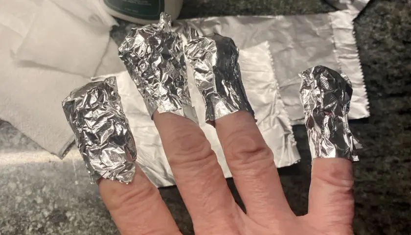 Fingrar inslagna i folie för att ta bort gellack hemma.