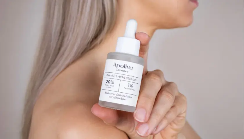 En hand håller en flaska med Apoliva PHA+AHA+BHA Peeling. Denna aha syra-produkt hjälper till att reducera döda hudceller.
