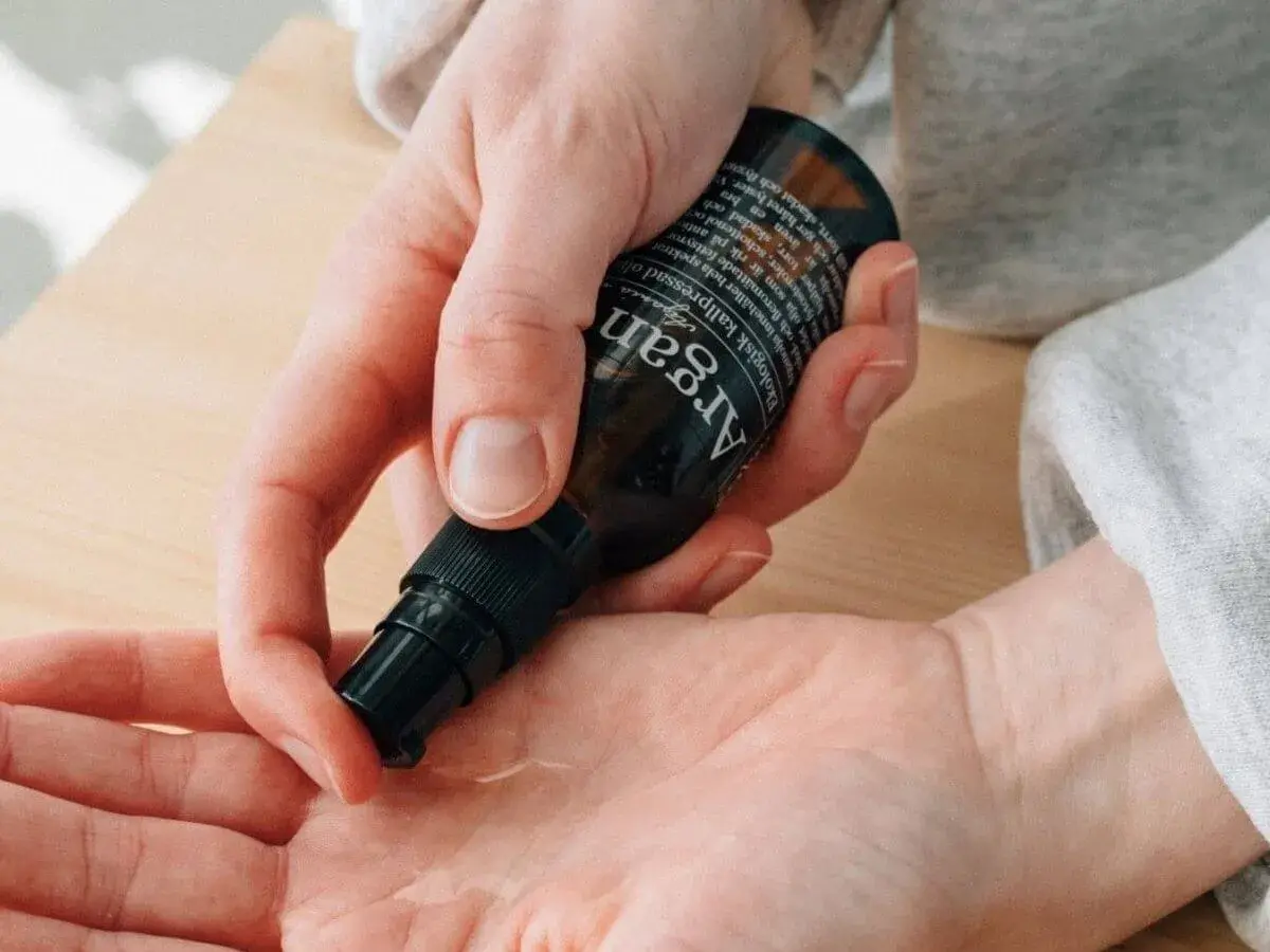En hand pumpar ut arganolja ansikte ur en mörk flaska. Oljan är ekologisk och kallpressad.