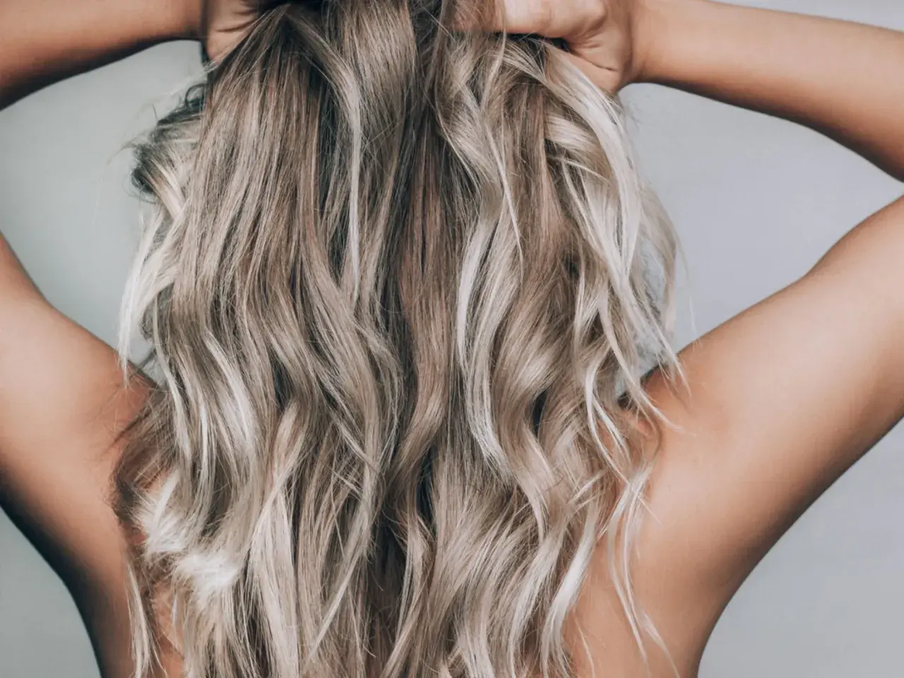 En person med blont, vågigt hår som håller om nacken. Håret ser ut att vara blekt med citron för en naturlig solkysst look.