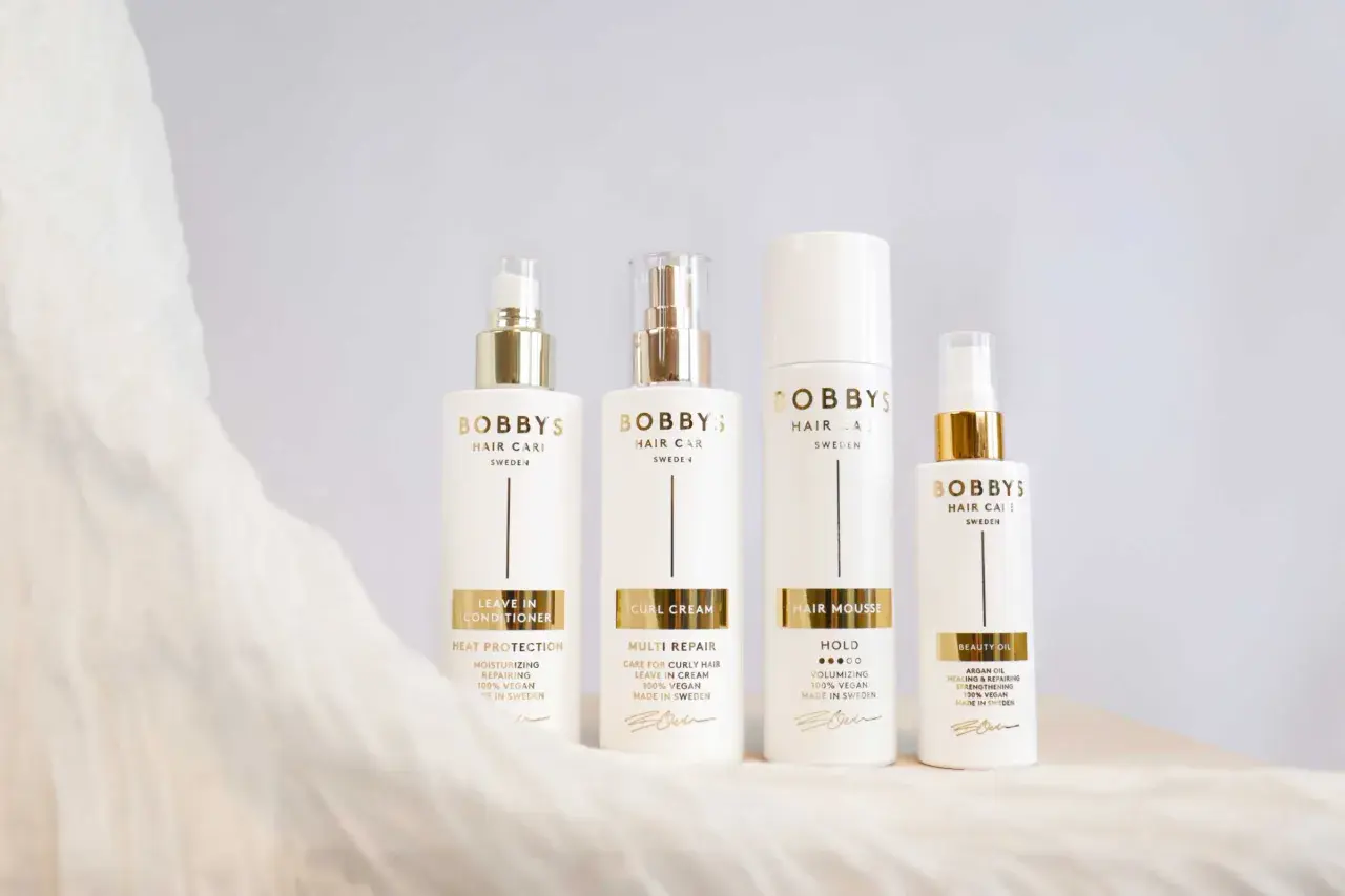 Fyra vita flaskor från Bobby's Hair Care med gulddetaljer. Produkterna hjälper mot statiskt hår och ger glans.