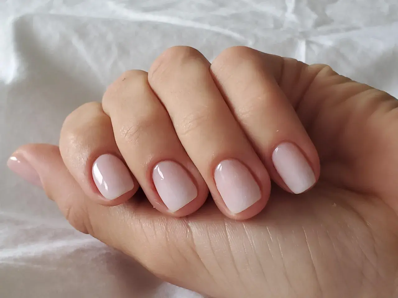 En hand med perfektionerad nagelbandsvård, en klassisk russian manicure med ljusrosa naglar som glänser.