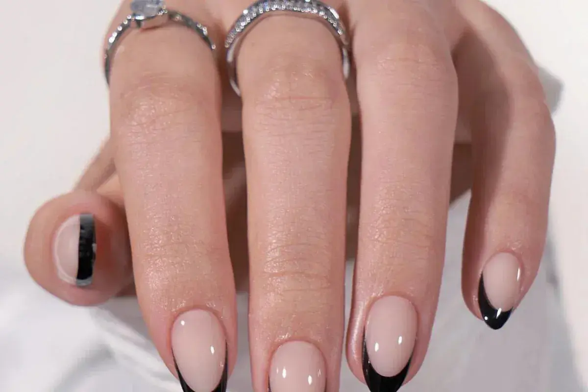 Ett par händer med eleganta press on nails i fransk manikyr med svarta spetsar. Två ringar pryder fingrarna.