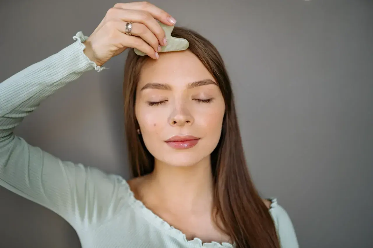 En kvinna med slutna ögon använder en gua sha för ansiktet, en del av hennes skönhetsrutin.