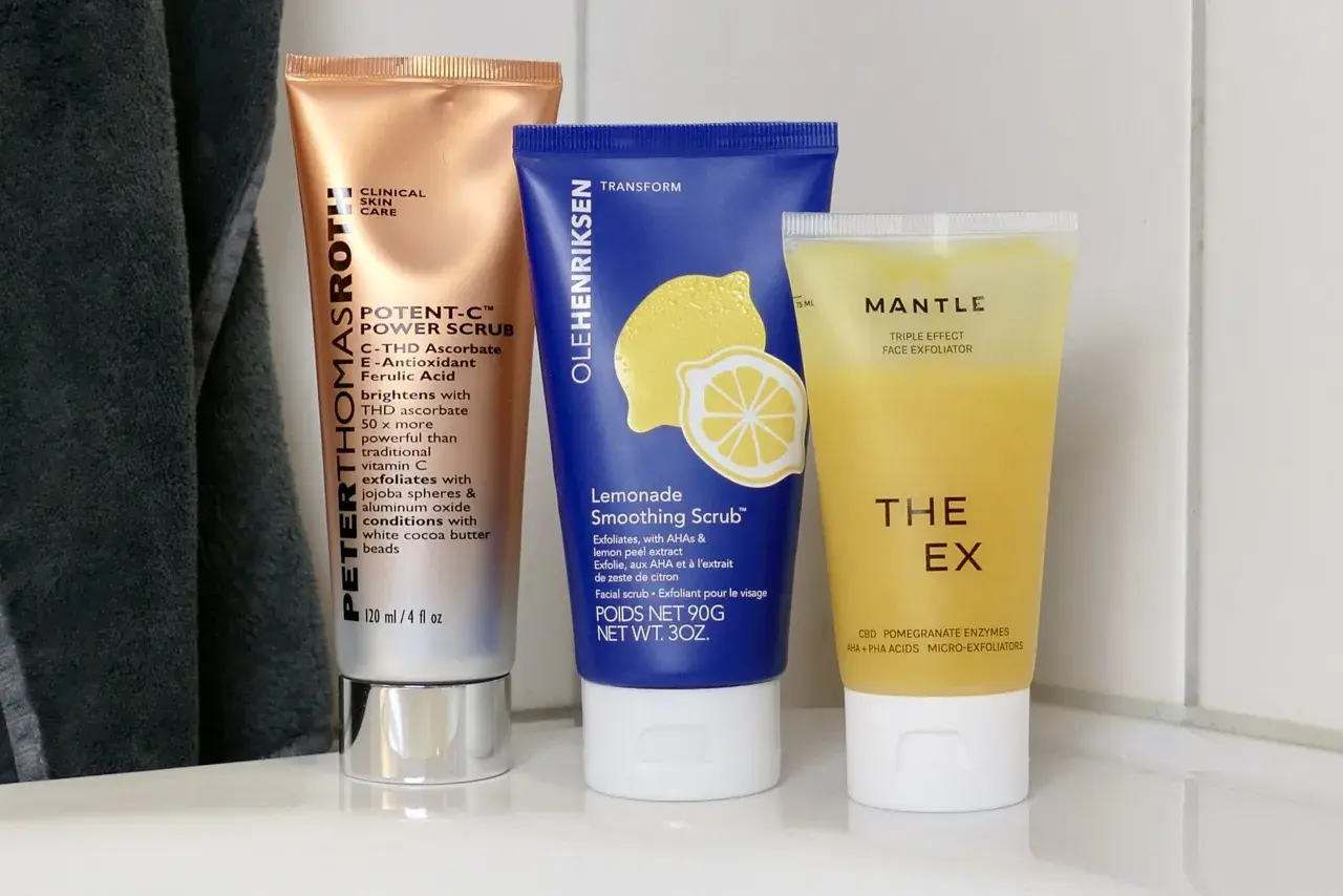 Tre tuber med ansiktsskrubb: en kopparfärgad, en blå med citron och en gul. Dessa produkter erbjuder mekanisk peeling för huden.