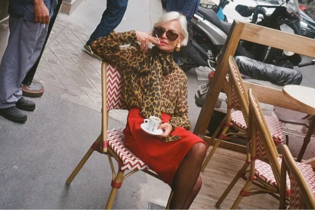 Elegant dam i leopardmönstrad blus och röd kjol, en kaffe i handen. En stil som inspirerar för vårmode 2026 dam.