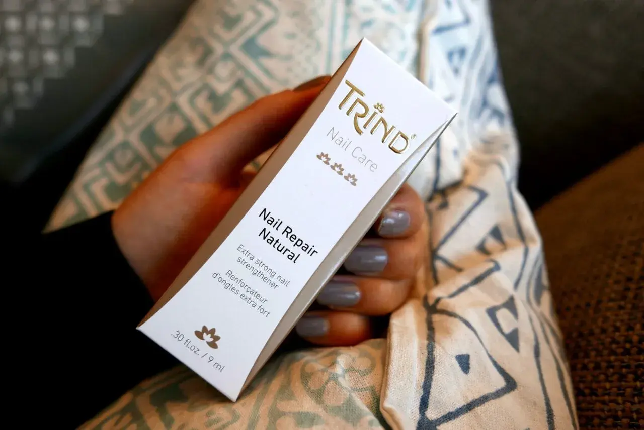 En hand håller en Trind Nail Repair Natural-förpackning. Produkten är inte farlig, utan en nagelförstärkare.