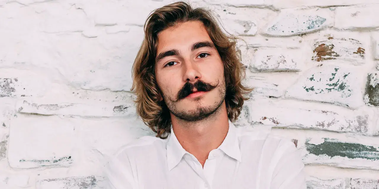 Ung man med långt hår och en imponerande mustasch som visar upp olika mustasch stilar.