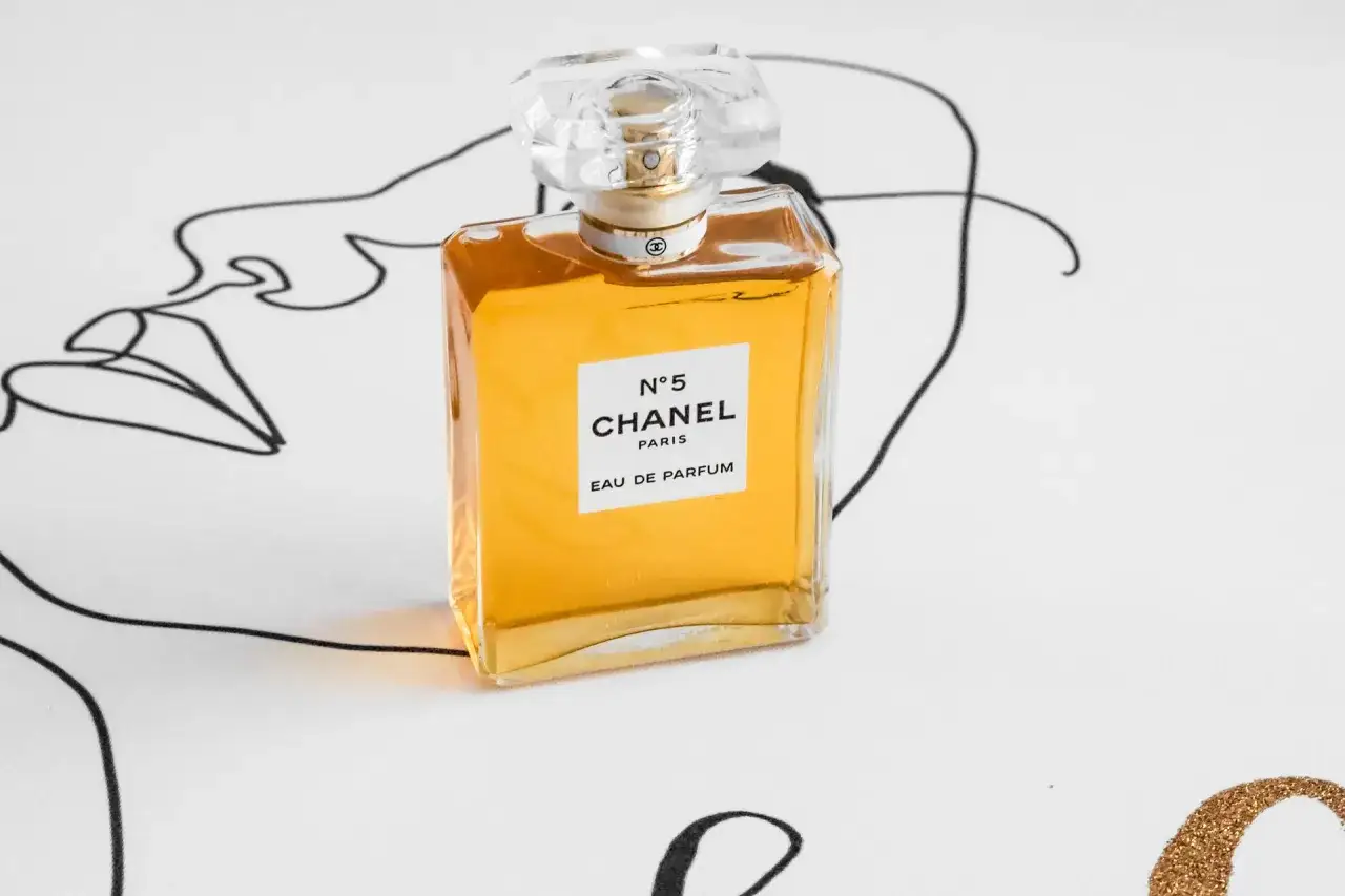 Chanel N°5 Eau de Parfum, en klassisk parfym för dam från 90-talet, står på ett tyg med en abstrakt ansiktslinjeteckning.