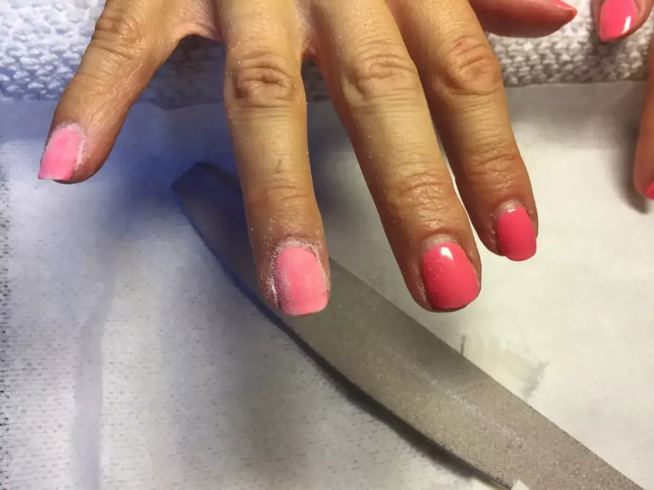 En hand med rosa gellackfilas för att ta bort gellack hemma. Naglarna är delvis filade, med synligt damm.