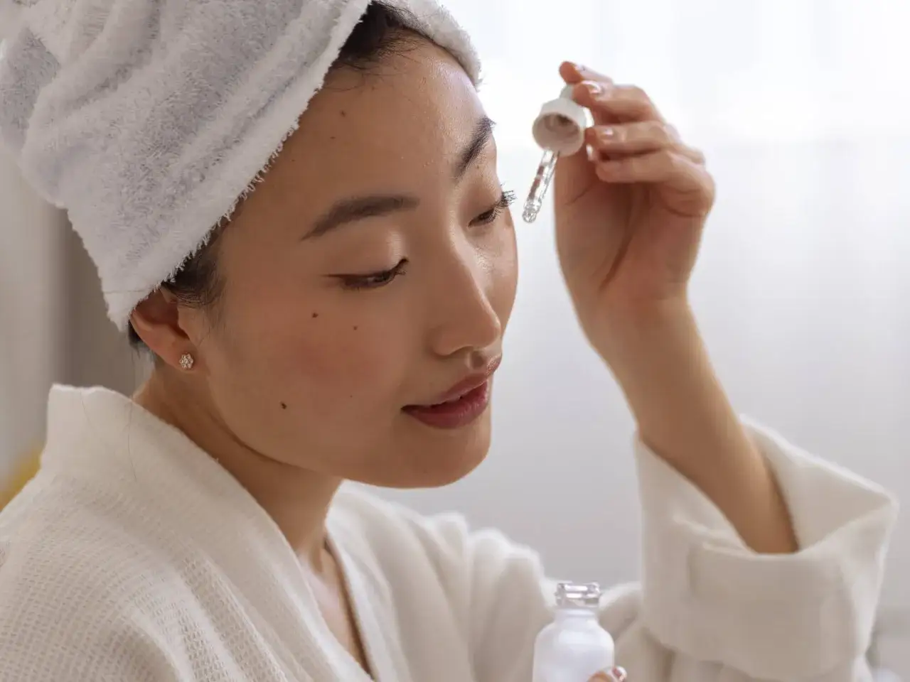 En kvinna med handduk i håret applicerar serum med pipett. Hennes hud strålar av j beauty.