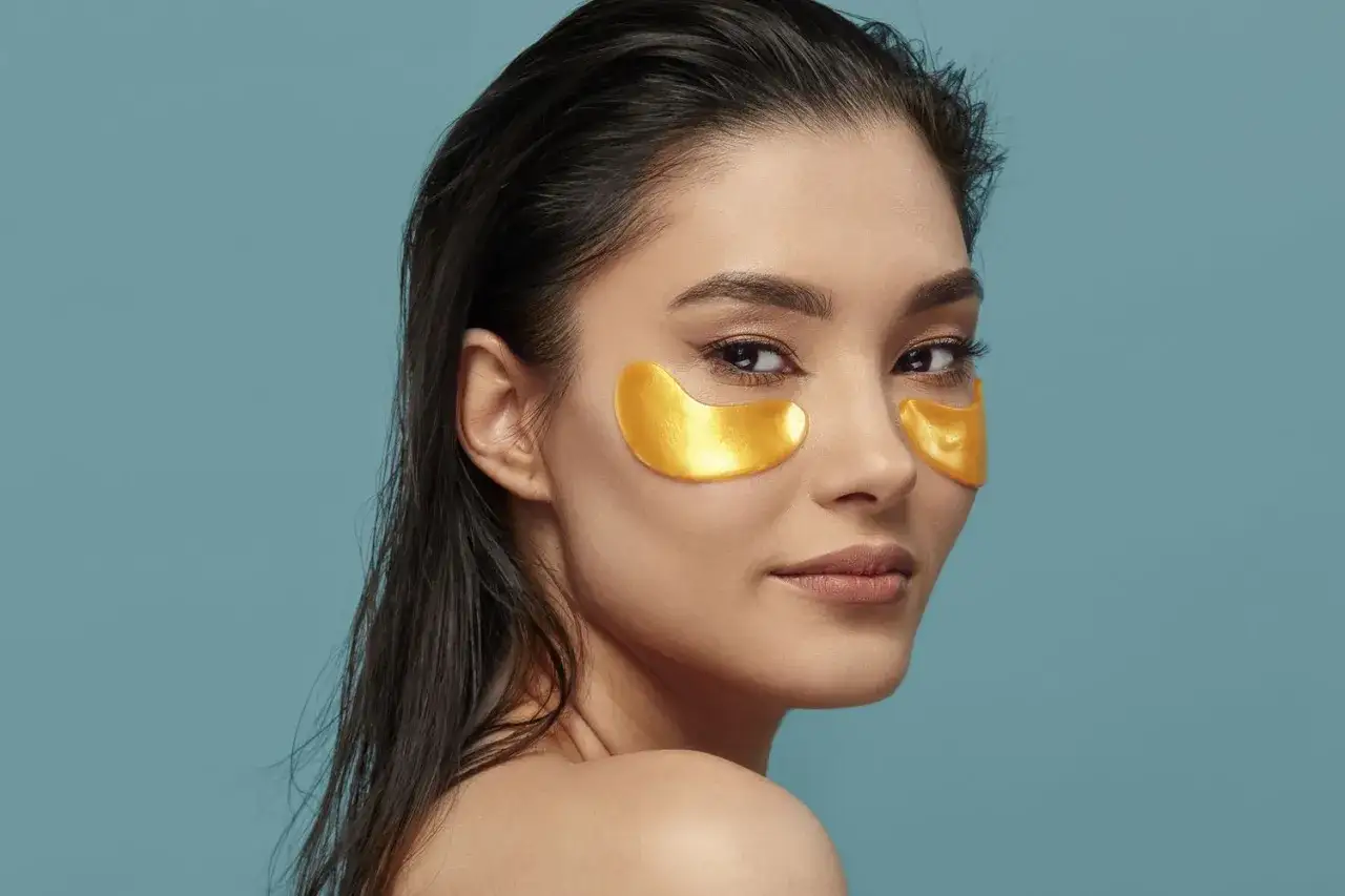 Kvinna med gyllene eye patches under ögonen, visar hur ska eye patches sitta för bästa resultat.