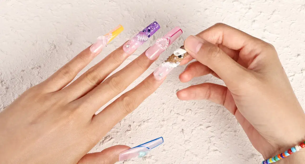 H&auml;nder med l&aring;nga, dekorerade press on nails i olika f&auml;rger och m&ouml;nster, som p&auml;rlor och sn&auml;ckor.