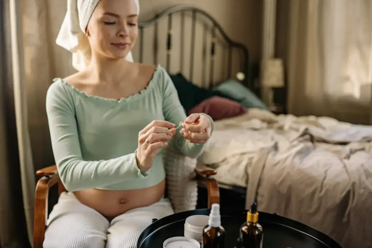 Gravid kvinna med handduk p&aring; huvudet tar hand om sin hud. Hon sitter i en stol med en s&auml;ng i bakgrunden.