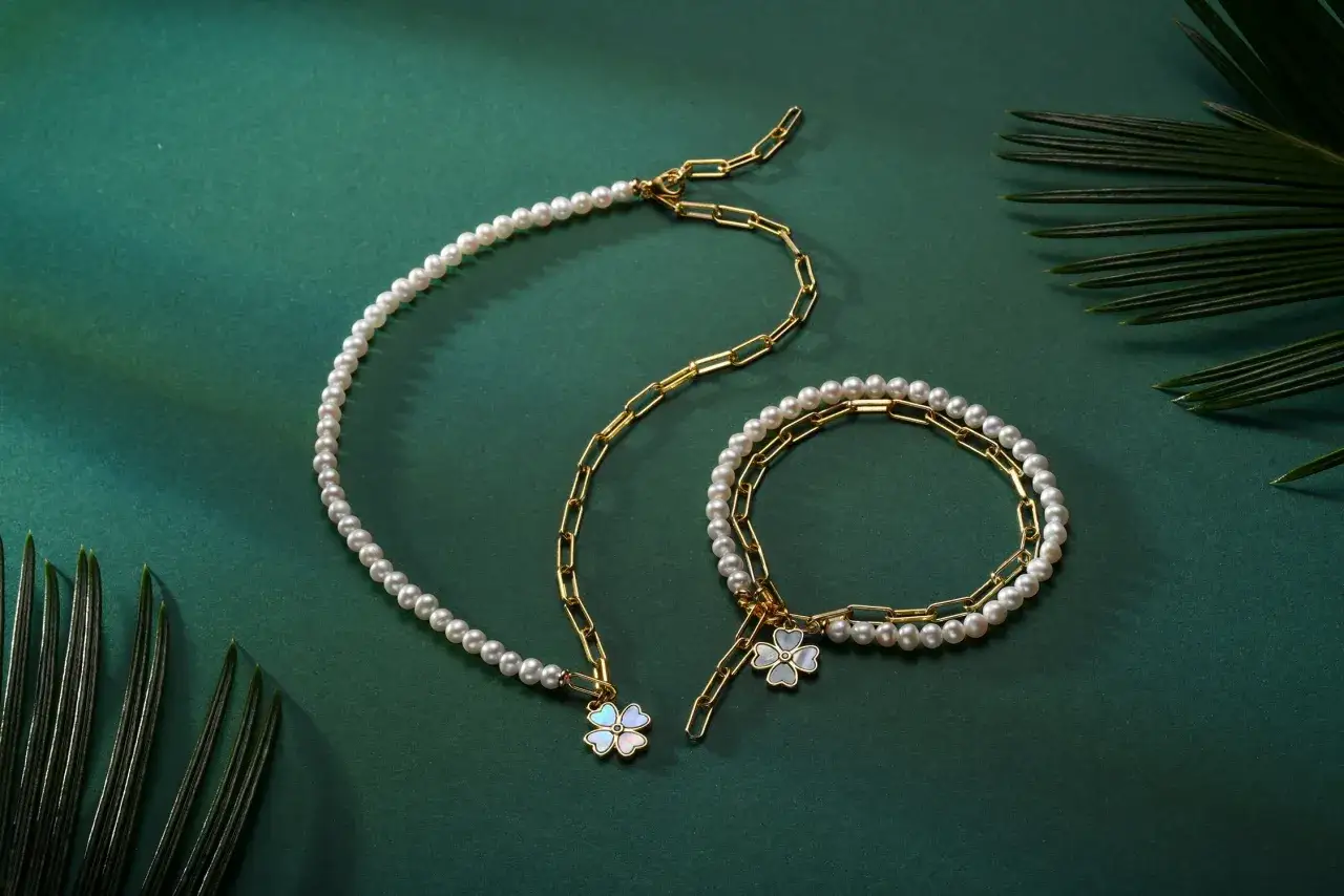 Ett halsband och ett armband med pärlor och guldkedjor, prydda med klöverformade berlocker. Moderna smycken som fångar ljuset.
