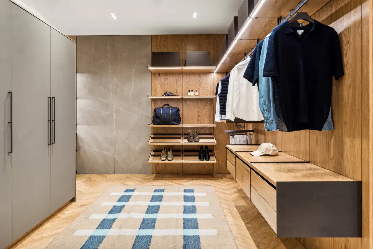 En walk-in-closet med tr&auml;detaljer, kl&auml;der p&aring; galgar och en matta. En k&auml;nsla av quiet luxury.
