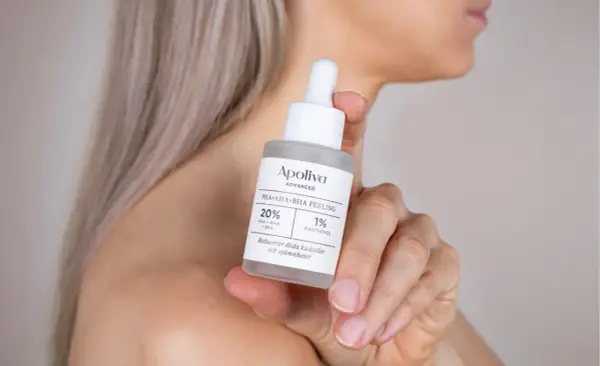 En hand håller en flaska med Apoliva PHA+AHA+BHA Peeling. Denna aha syra-produkt hjälper till att reducera döda hudceller.